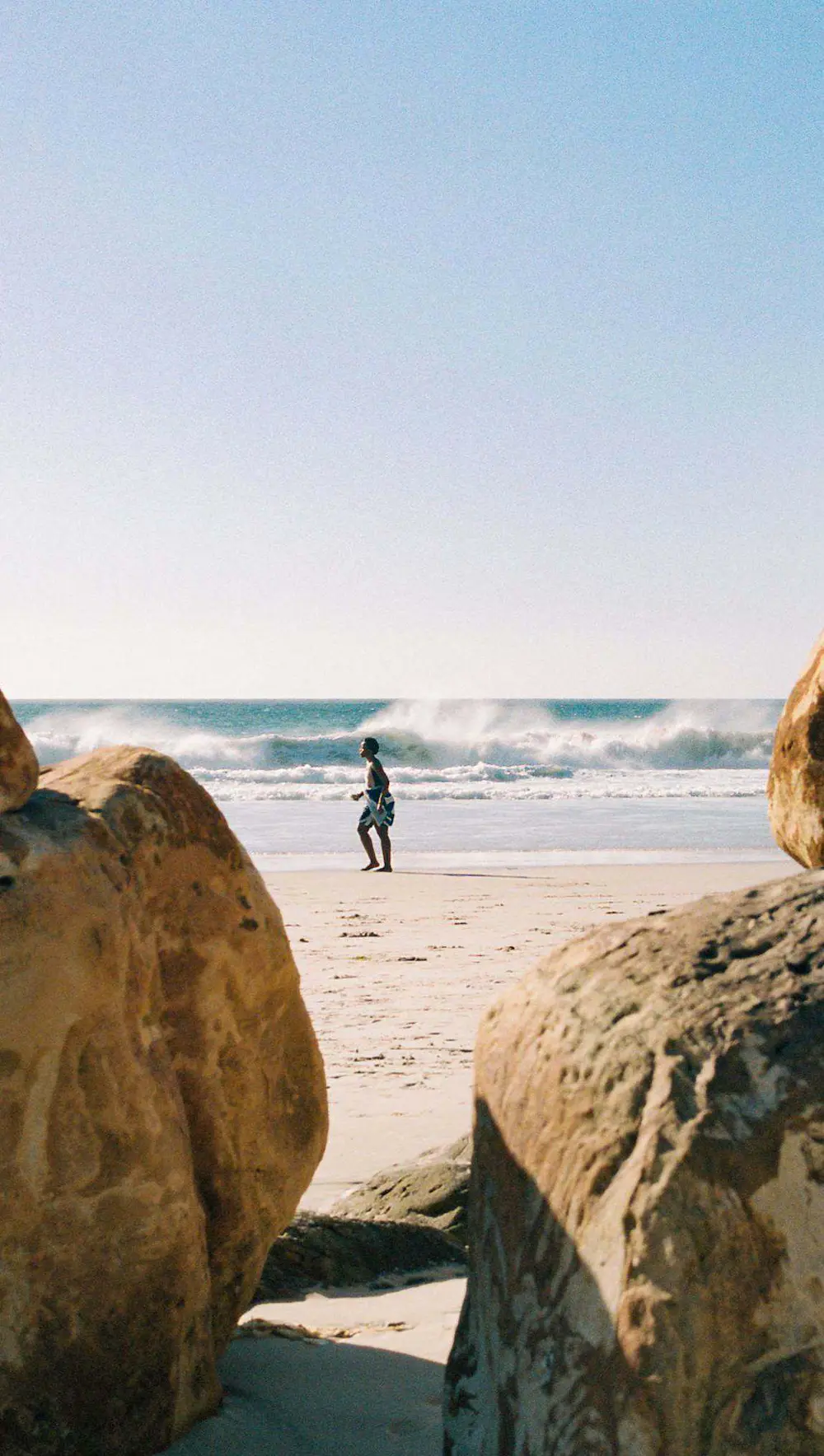 Un voyageur marche sur une plage entre deux rochers