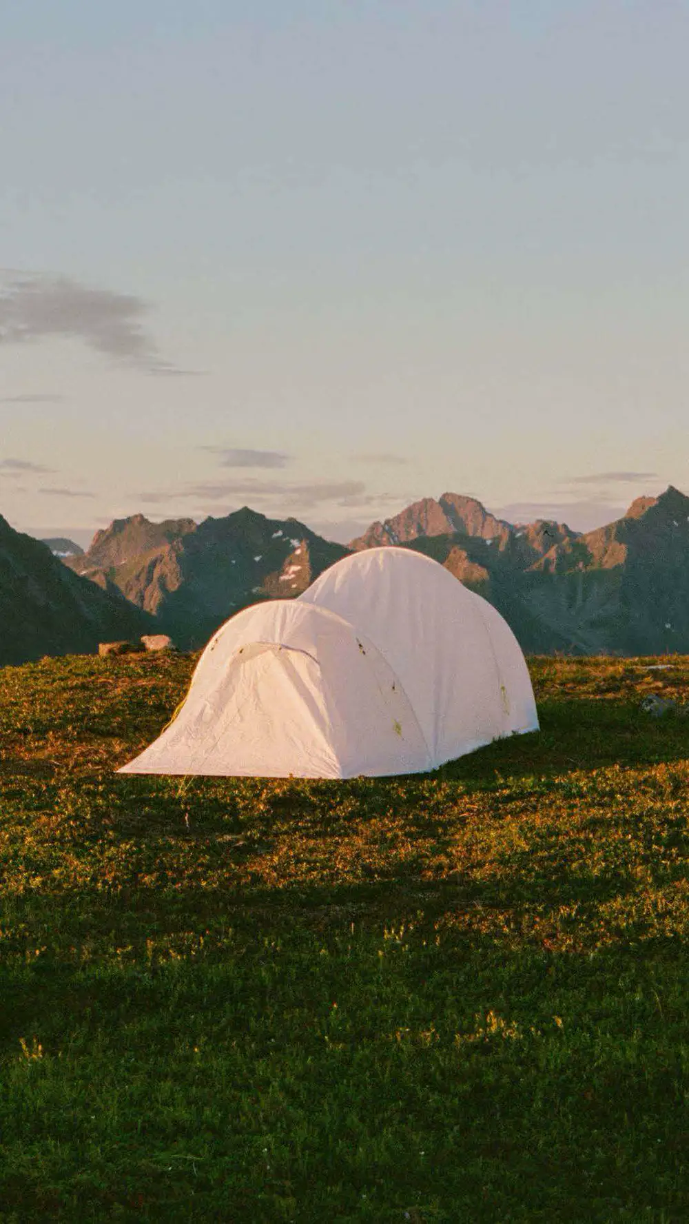 Une tente blanche face aux montagnes au coucher du soleil
